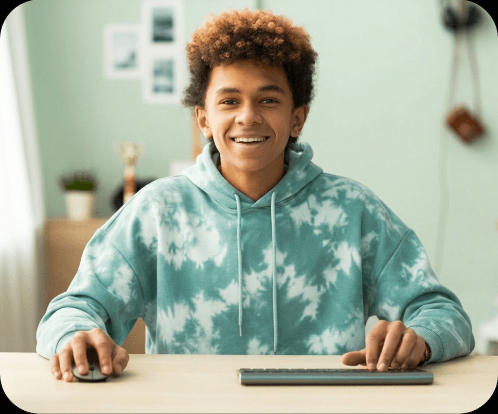 Teenage student in a tie-dye hoodie smiling while working at a computer